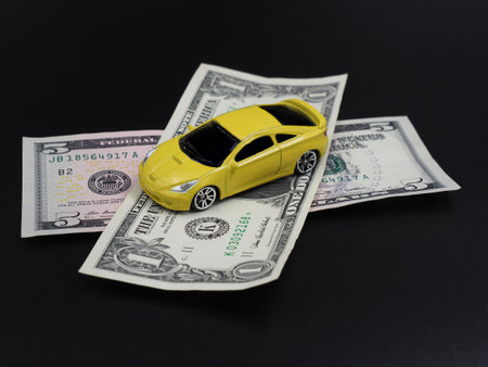 Buying or renting a car. Car sharing. Yellow toy car on dollar bills on a black gradient background. Collapse of prices, discount on the car.の写真素材