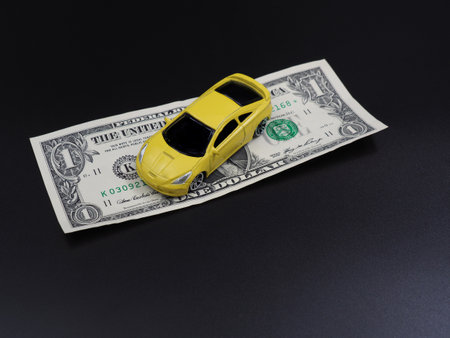 Buying or renting a car. Car sharing. Yellow toy car on dollar bills on a black gradient background. Collapse of prices, discount on the car.の写真素材