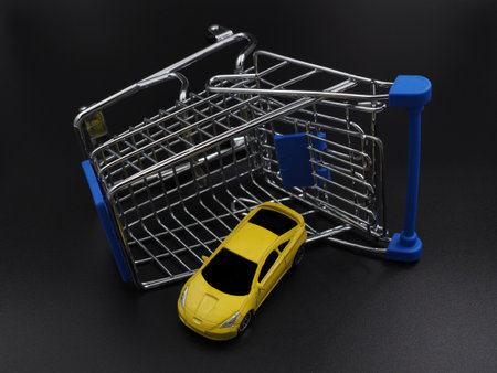 Buying or renting a car. Car sharing. Yellow toy car in a shopping cart on a black gradient background. Collapse of prices, discount on the car.の写真素材