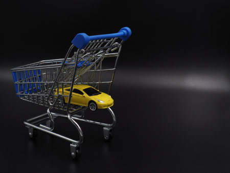 Buying or renting a car. Car sharing. Yellow toy car in a shopping cart on a black gradient background. Collapse of prices, discount on the car.の写真素材