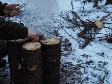 A man throws a hand into the campfire "Finnish candle" kindling in the form of small twigs. Lighting a fire in the winter forest in a campfire. The concept of survival in extreme conditions.の写真素材