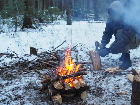 A man without a face is chopping wood in the smoke from a campfire. a woodcutter splits a log for a fire in the winter forest. The shish kebab, barbecue weekend.の写真素材