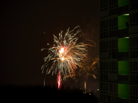 New Year or Christmas salute in the Russian suburbs. A smoking man on the balcony of a high-rise building, a skyscraper looks at the fireworks.の写真素材