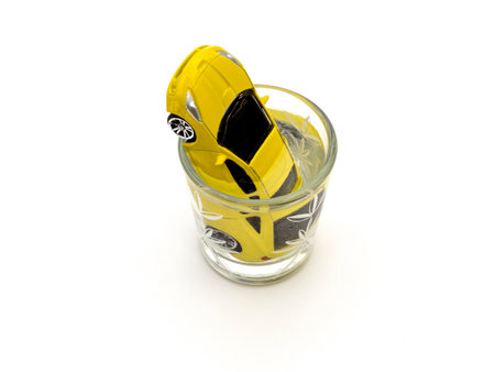 Yellow car drowned in a glass of alcohol on a white background. Social advertising. The concept of...