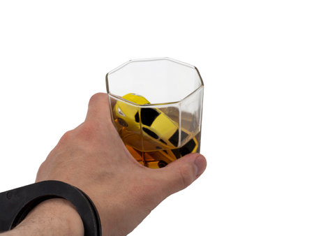 A man's handcuffed hand holds a car drowning in a glass of whiskey. The concept of social advertising, arrest for drunk driving. Studio photo isolated on a white background.の写真素材