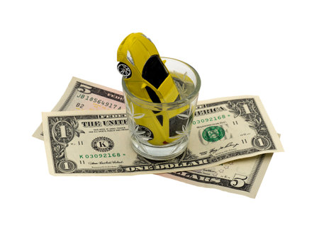 A yellow car is drowning in a glass of alcohol on dollar bills. Mac-up. Social advertising. Concept of drunk driving, car accident, financial expenses for the car.の写真素材