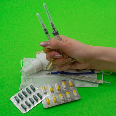 The girl holds a fist over medical preparations, tablets, an electronic thermometer, a mask, an antiseptic, a vaccine and syringes. The concept of expensive treatment after coronavirus infection.の写真素材