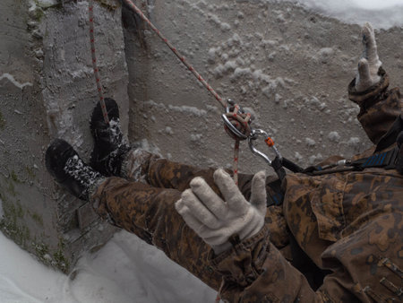 A military mountaineering instructor teaches climbing knots from a rope with a carbine and "figure 8" on a sheer wall. A man in camouflage shows a "Horned eight" close-up, hands in white gloves.の写真素材