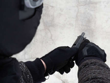 A man wearing black tactical gloves and a Russian assault helmet with a visor, holds and reloads a...