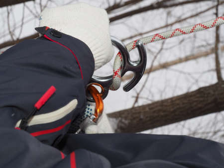 The athlete climber is preparing for the descent. The man ties the rope around the carbine and the "figure-eight descender" in a knot. Mountaineering equipment close-up.の写真素材