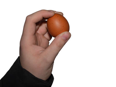 A man holds a raw chicken egg in his hand and prepares to throw it. The concept of choosing products for the Easter holiday.の写真素材