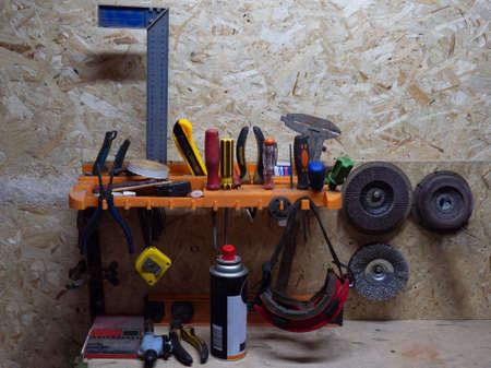 Shelf with tools in garage against the background of plywood made of pressed sawdust. Wrench,...