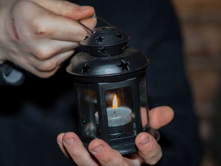 A man in two dirty, working hands holds a candle in a closed candlestick. The concept of a heating point in a shelter, helping the homeless and the poor.の写真素材