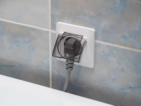 White electric socket with transparent gray cover and plug in the bathroom on the background of the...