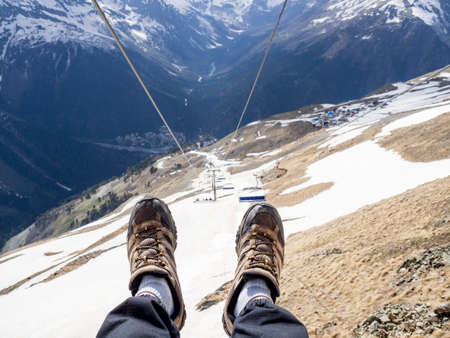 First person view of men feet in sneakers while descending an open cable car. Chairlift with empty...