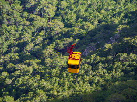 Yellow cab of a passenger funicular lifts tourists on a cable car against background of a green forest. Bright, summer contrast photo. Close-up, top view. Crimea, a mountain of the Ai-Petri plateau.の写真素材