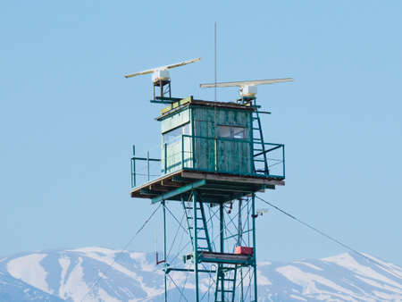 Technical observation post on shore of bay on background of mountains. Lonely building behind a barbed wire fence with a radar tower and a cell tower. Crimea. Small border post, a weather station.の写真素材