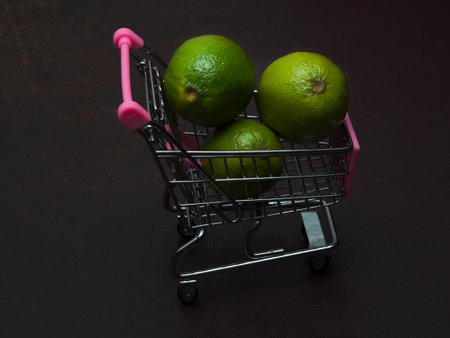 One green sour lime is in a small shopping trolley. An exotic tropical fruit in a toy metal cart. The concept of autumn harvest and sale.の写真素材