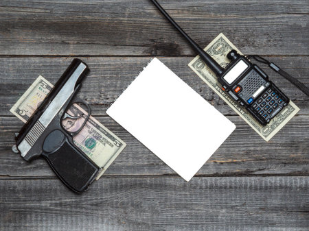 A portable radio with dollar bills and a pistol on a wooden table background. Copy space white notepad. The concept of police corruption, black market, money crimes.の写真素材