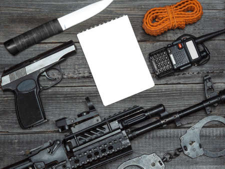 A combat automatic rifle, a police pistol and a portable radio on a wooden background of a table...