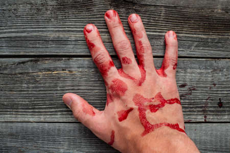 A dead man holds a police pistol in his bloody hand on a wooden background of a table or floor.の写真素材