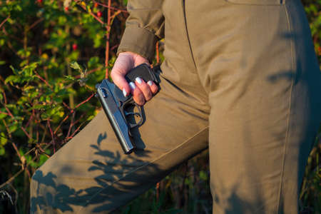 A girl in a green military jumpsuit stands against the background of red bushes and rosehip berries...