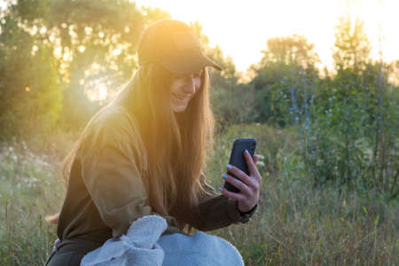 A young girl on a trip shares her impressions via a live broadcast on the Internet with friends or subscribers. A female tourist in a green jumpsuit laughs, smiles and talks on the phoneの写真素材