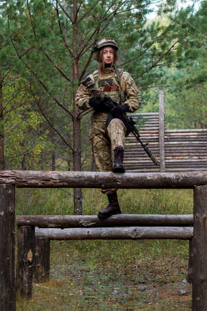 A girl in military equipment passes an obstacle course in a forest camp at an army training ground.