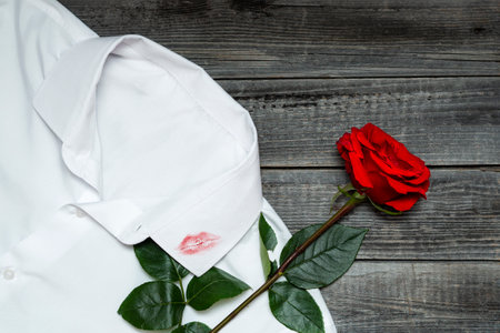 A trace of lipstick lips from a kiss on men's clothing. One red rose lies on a white shirt on a rough wooden background. Infidelity and romance.の写真素材