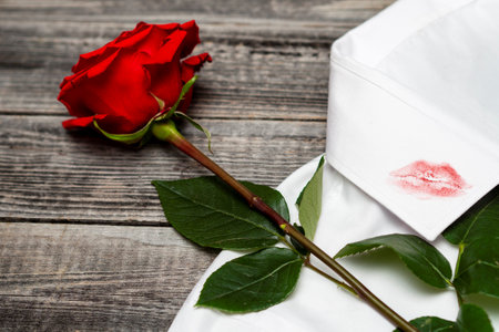 A trace of lipstick lips from a kiss on men's clothing. One red rose lies on a white shirt on a rough wooden background. Infidelity and romance.の写真素材