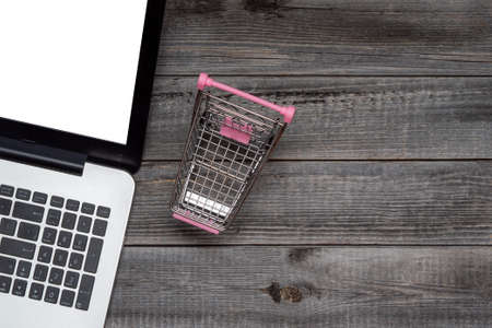 Laptop against the background of a gray wooden table next to an empty shopping cart. Flat lay, top view. Concept of online shopping on Black Friday and Cyber Monday.の写真素材