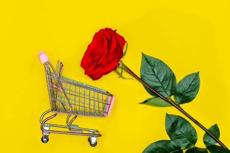 A red rose next to a shopping cart on a yellow background. The concept of Valentine's Dayの写真素材