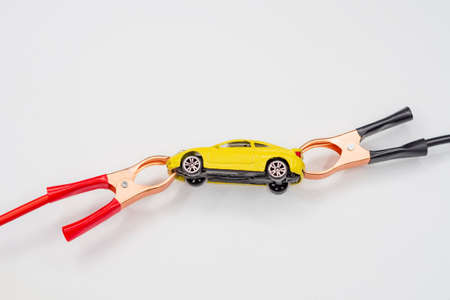Red and black wire automotive clips or battery clamps on a yellow toy car on a white background. The concept of a quick start of the battery, starting the automobile engine in winter.の写真素材
