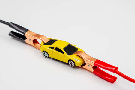 Red and black wire automotive clips or battery clamps on a yellow toy car on a white background. The concept of a quick start of the battery, starting the automobile engine in winter.の写真素材