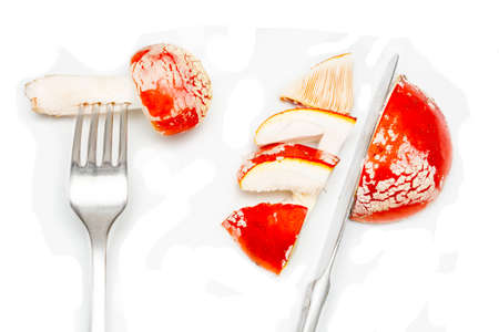 Red fly agaric (amanita muscaria) on a white background with cutlery fork and knife. The concept of poisoning mushroom toadstool, the use of hallucinogens and drugs.の写真素材