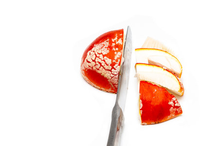 A red fly agaric (amanita muscaria) hat cut into pieces with a table knife on a white background. The concept of poisoning mushroom toadstool, the use of hallucinogens and drugs.の写真素材