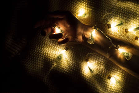 Male rough hand wrapped with merry Christmas tree garlands of glass jars on the background of a knitted white sweater. Winter holiday comfort and expression.の写真素材