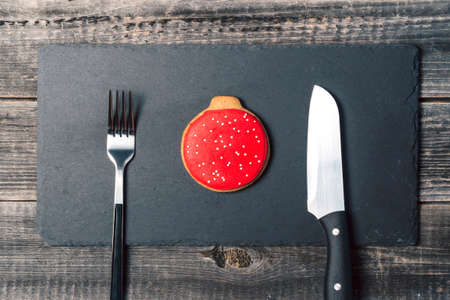 Ginger cookies in the form of a red ball Christmas tree decoration lies on a black slate board with a serving fork and knife on a wooden board table background. Concept of Christmas dinner.の写真素材