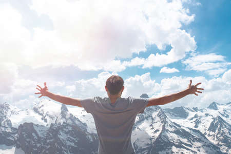 A man in a gray T-shirt poses against the background of snow-covered rocks. A view from the back of...