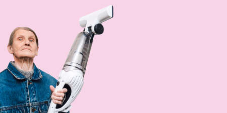 Proud elderly woman poses with a new handheld vacuum cleaner, the photo is isolated on a pink pastel background.の写真素材