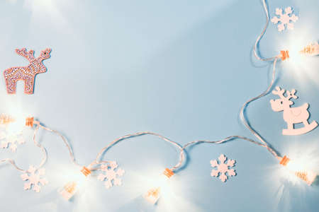 Christmas flat lay with a garland of bottles, a toy wooden deer and white snowflakes on a blue background. Copy space, a place to insert text.の写真素材