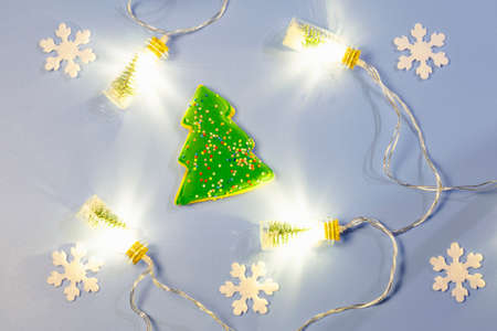 Christmas flat lay with a garland of bottles, ginger cookies in the form of a green fir tree and white snowflakes on a blue background.の写真素材