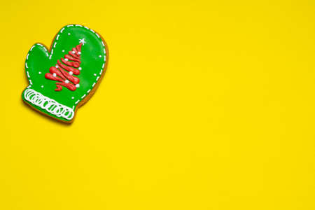 Christmas ginger cookies in the shape of a green mittens with a Christmas tree on a yellow background. Copy space, a place to insert text.の写真素材
