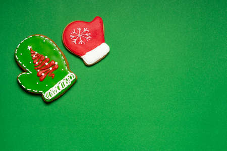 Christmas ginger cookies in the shape of a two green and red mittens on a green background. Copy...