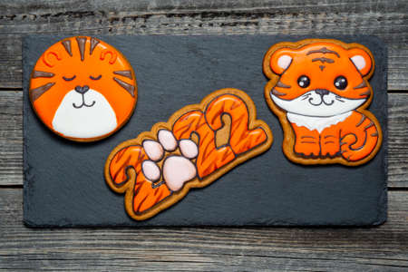 A Christmas ginger cookie in the shape of a tiger and the numbers 2022 in tiger coloring lies on a black kitchen slate board.の写真素材