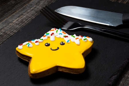 Christmas ginger cookies in the form of a yellow star decoration on a black kitchen slate board next to a serving knife and fork.の写真素材