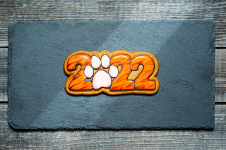 Christmas ginger cookie with the numbers 2022 in tiger coloring lies on a black kitchen slate board.