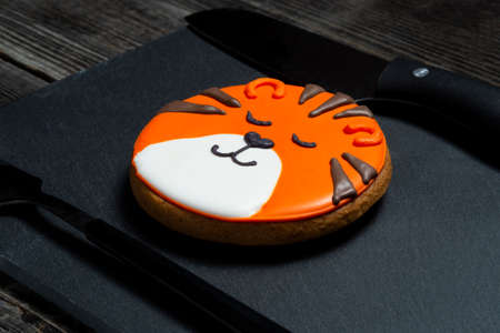 A Christmas ginger cookie in the shape of a tiger ball lies on a black kitchen slate board next to a...