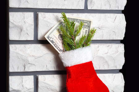 A red Christmas stocking filled with dollar bills stands against a brick wall by the fireplace. A small amount of money. The concept of a Christmas gift during a crisis.の写真素材