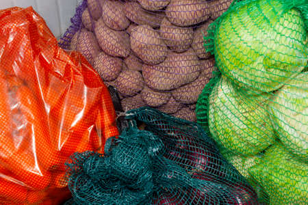 Carrots, cabbage, onions and potatoes in bags in a warehouse in the market close-up. The concept of collecting selling and buying vegetables.の写真素材